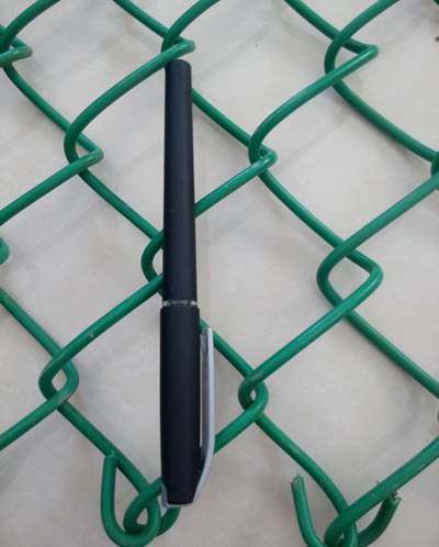 Un stylo noir est placé sur le PVC vert a enduit la barrière de maillon de chaîne et la longueur de deux trous est équivalente avec la longueur d'un stylo.